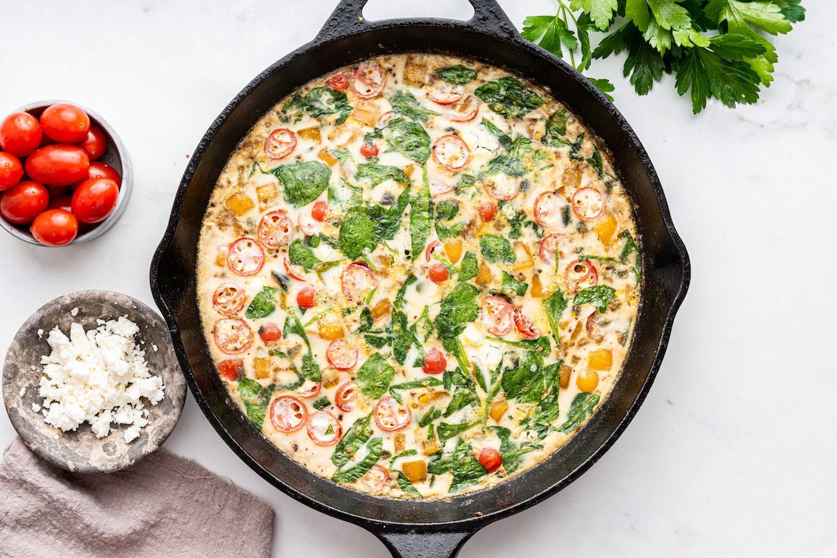 An egg white frittata after being cooked in a cast iron skillet. The frittata has spinach, cherry tomatoes, bell pepper, and red onion.