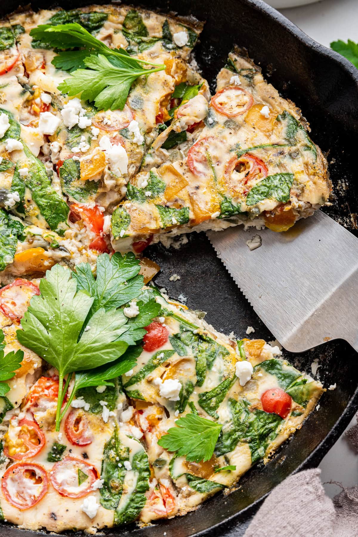 A serving spatula is removing a slice of egg white frittata from a cast iron skillet.