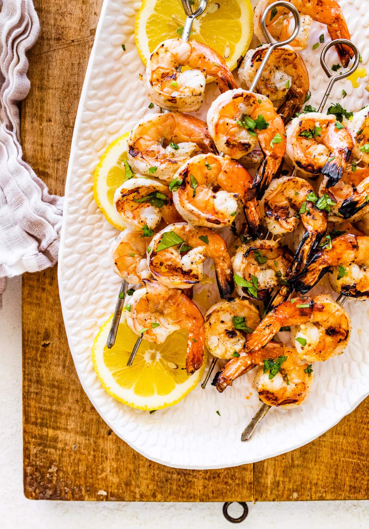 Multiple grilled shrimp skewers on a large white plate with lemon slices.