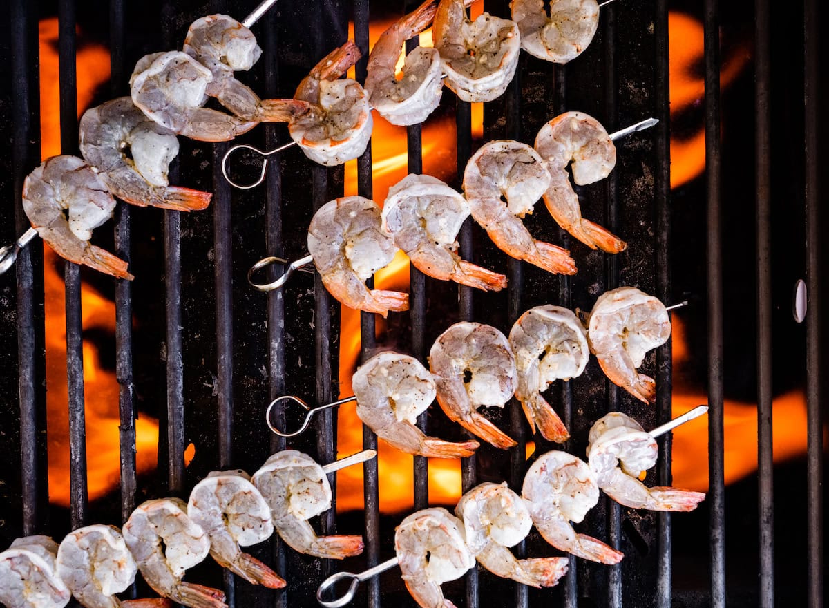 Raw shrimp on metal skewers over a grill.