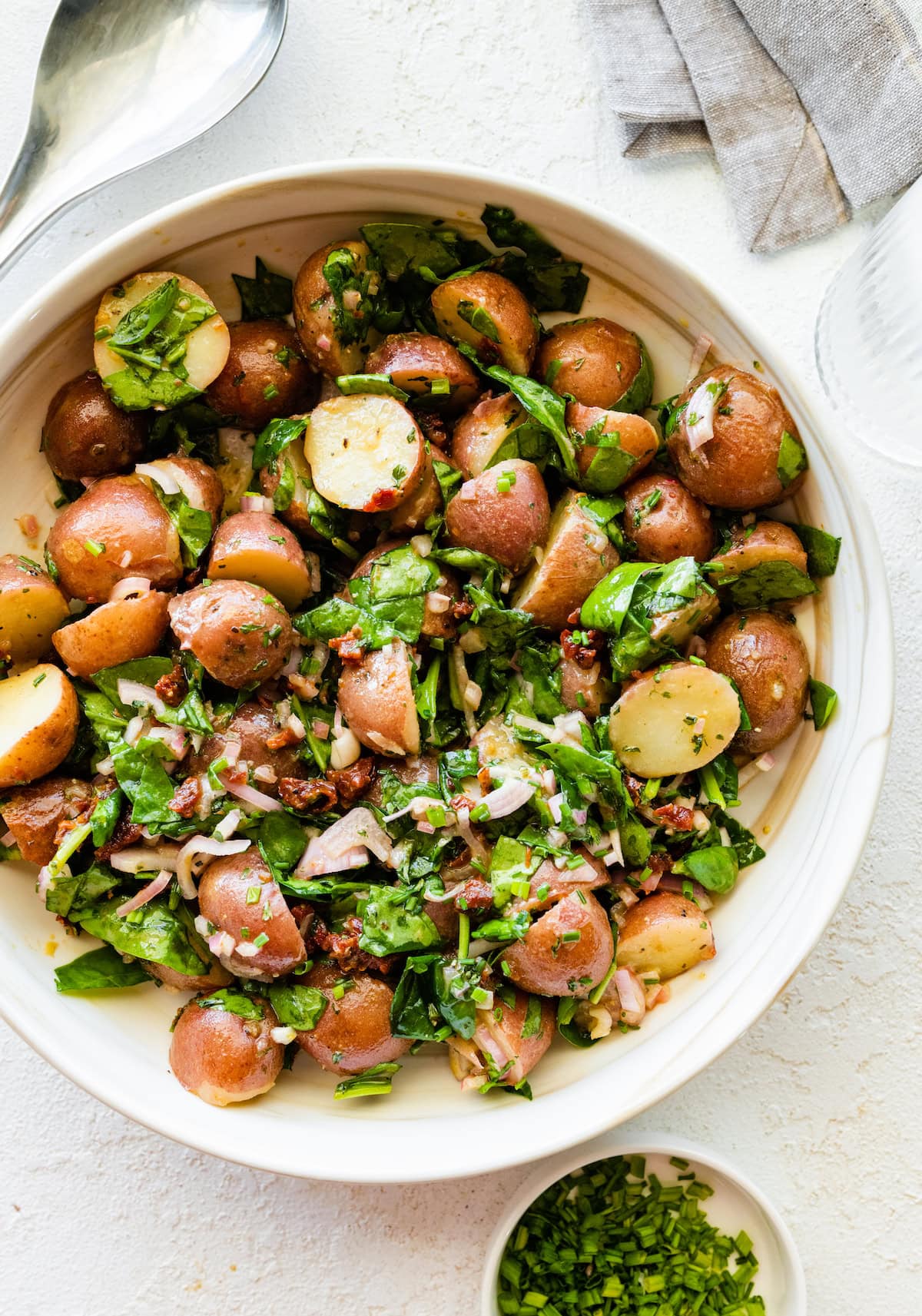 A serving of no may potato salad with cooked potatoes, spinach, onion, sun dried tomatoes, and fresh herbs.