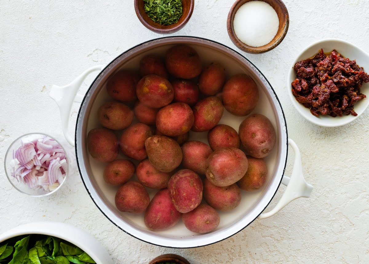 Multiple fingerling potatoes in a large pot of water.