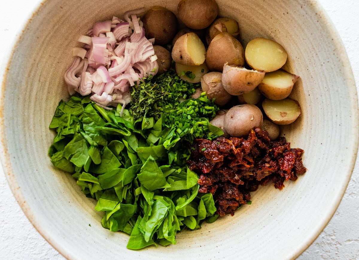 Potatoes, bacon, spinach, herbs, and sun dried tomatoes in a large mixing bowl.