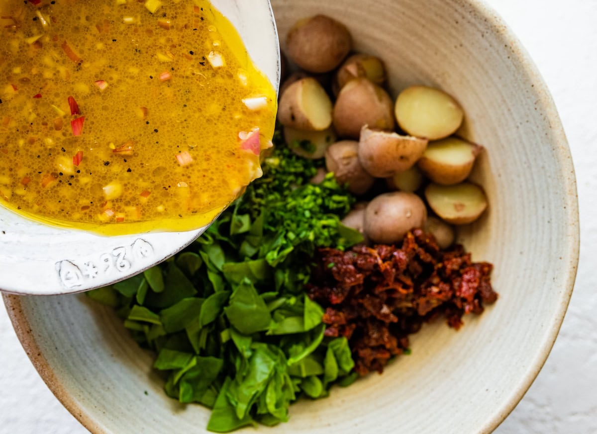 Dressing is being poured over a large bowl of ingredients for the no mayo potato salad.