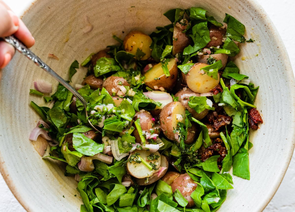 A woman's hand uses a fork in a large bowl of a no mayo potato salad.