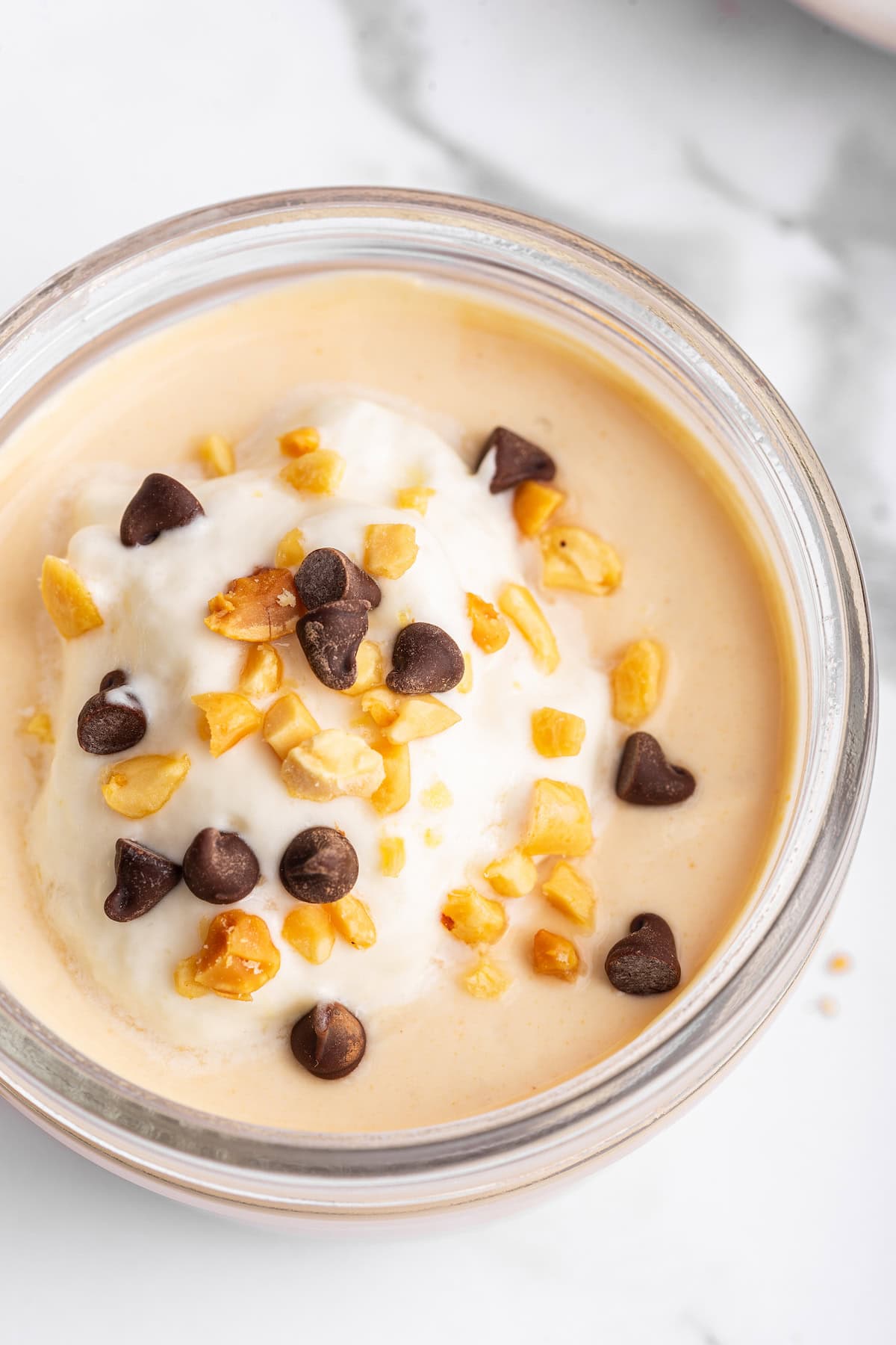 Peanut butter protein pudding in a glass container topped with mini chocolate chips, chopped peanuts, and yogurt.