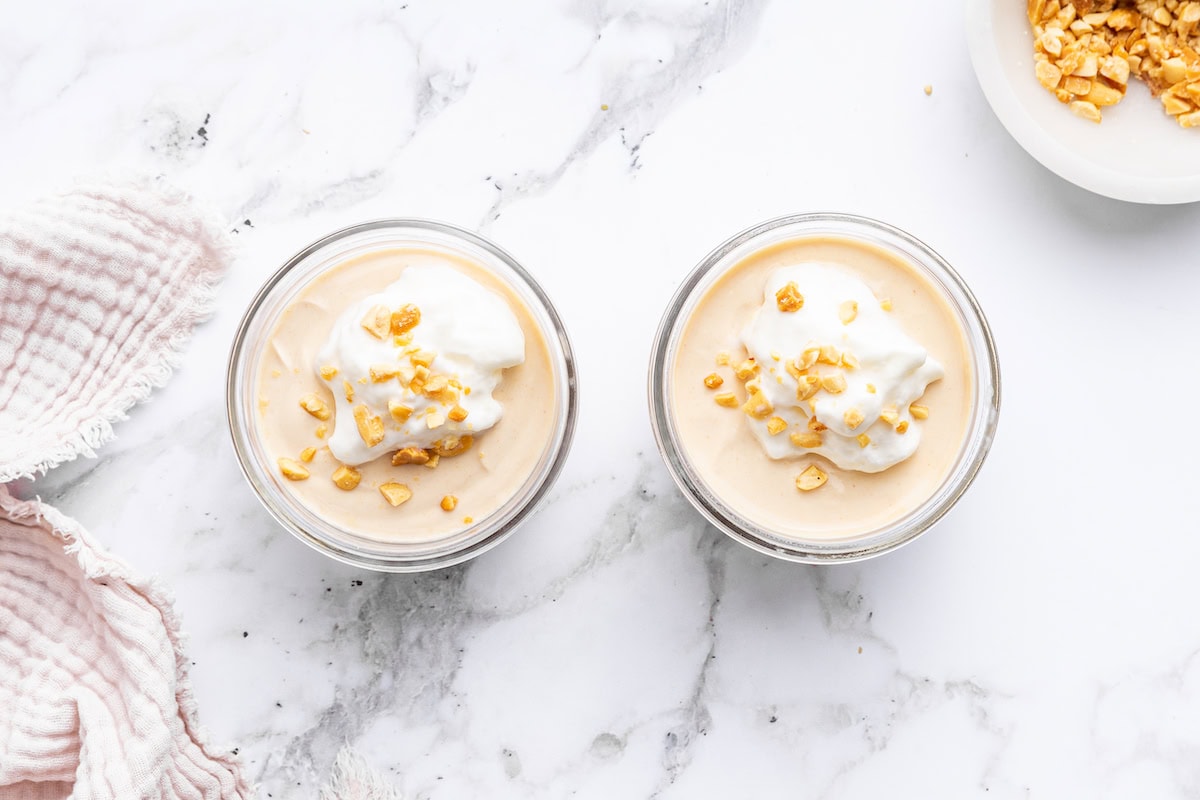 Two glass containers of peanut butter protein pudding topped with yogurt and crushed peanuts.