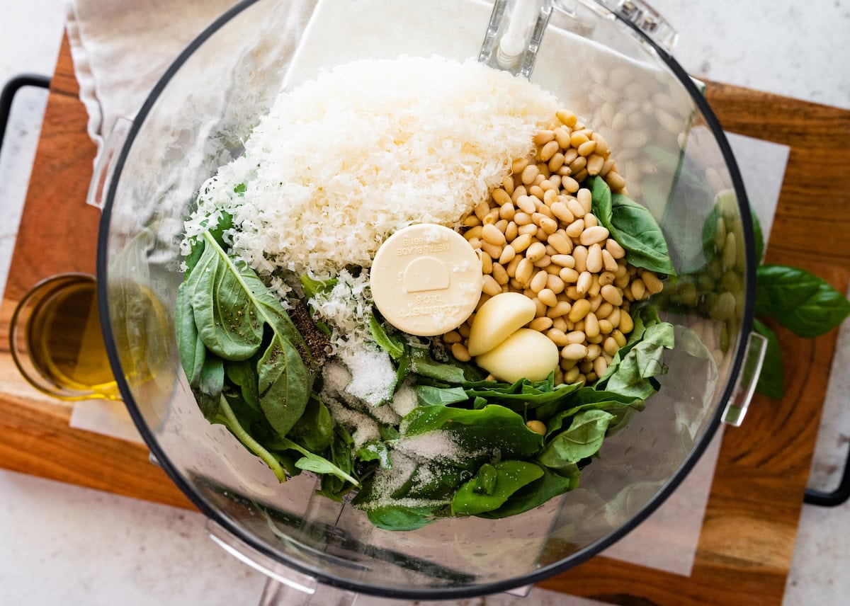 Pesto ingredients (pine nuts, garlic, basil, parmesan cheese and salt) in the bowl of a food processor before being blended.