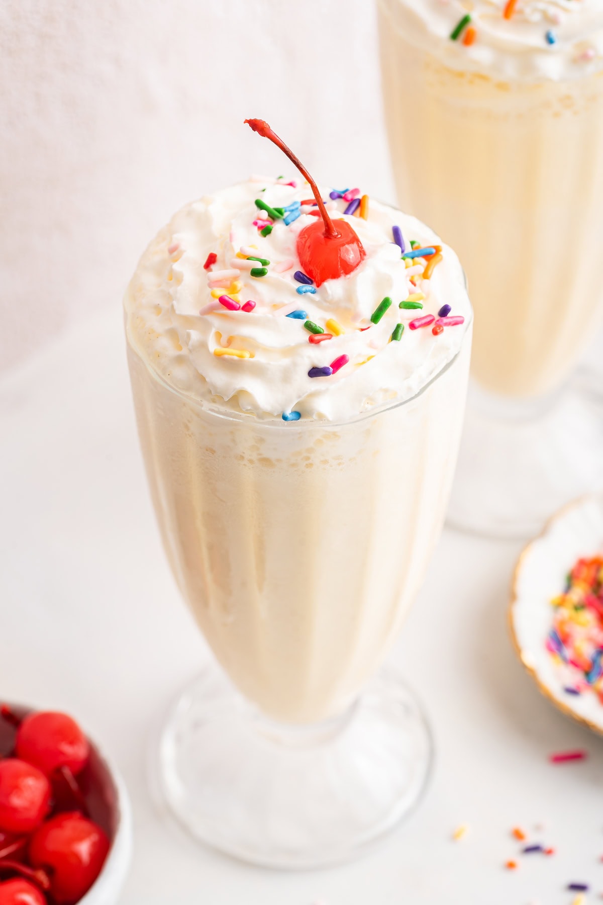 A protein milkshake in a large glass cup topped with whipped cream, sprinkles, and a cherry.
