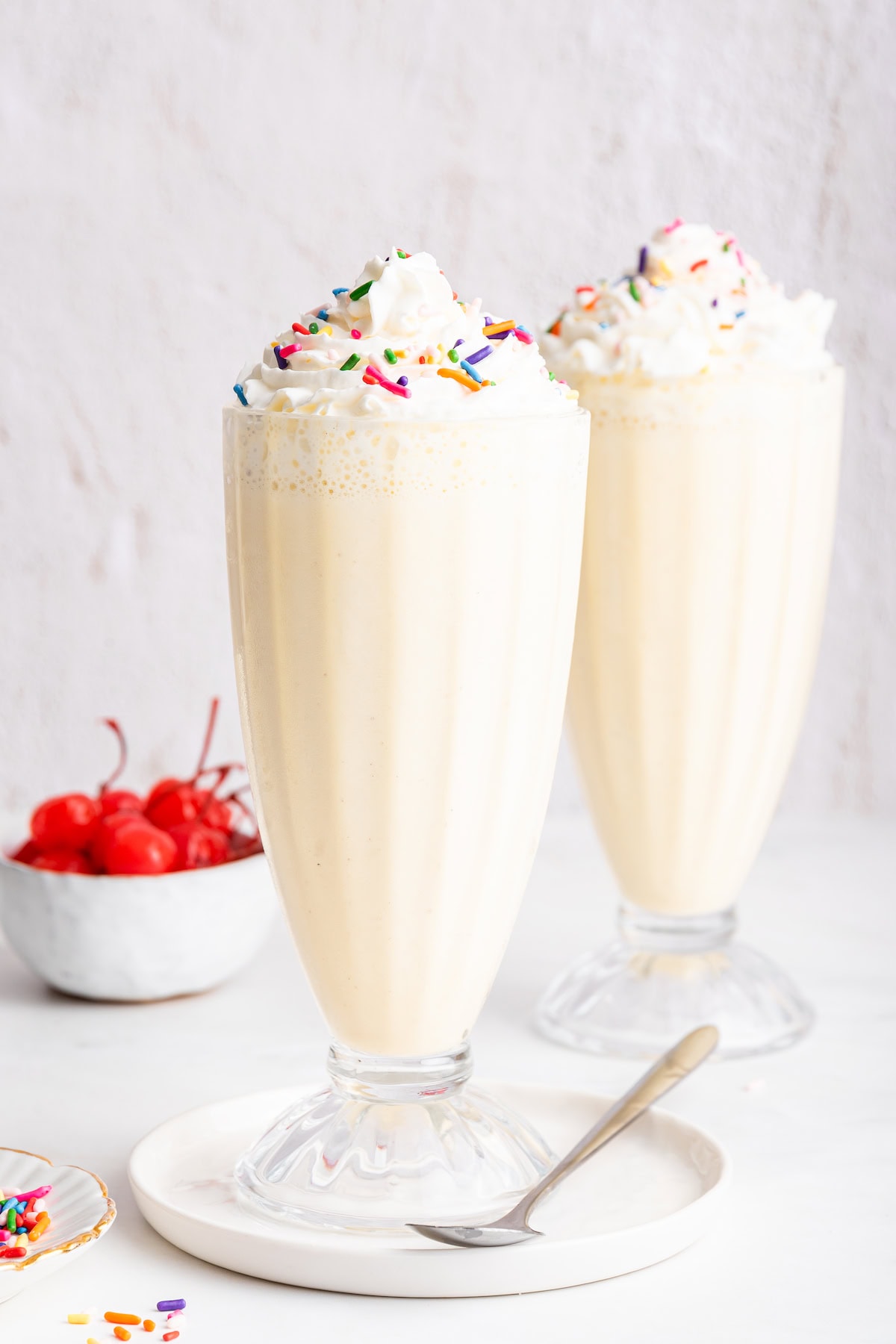 Two protein milkshakes in glass cups topped with whipped cream and sprinkles.