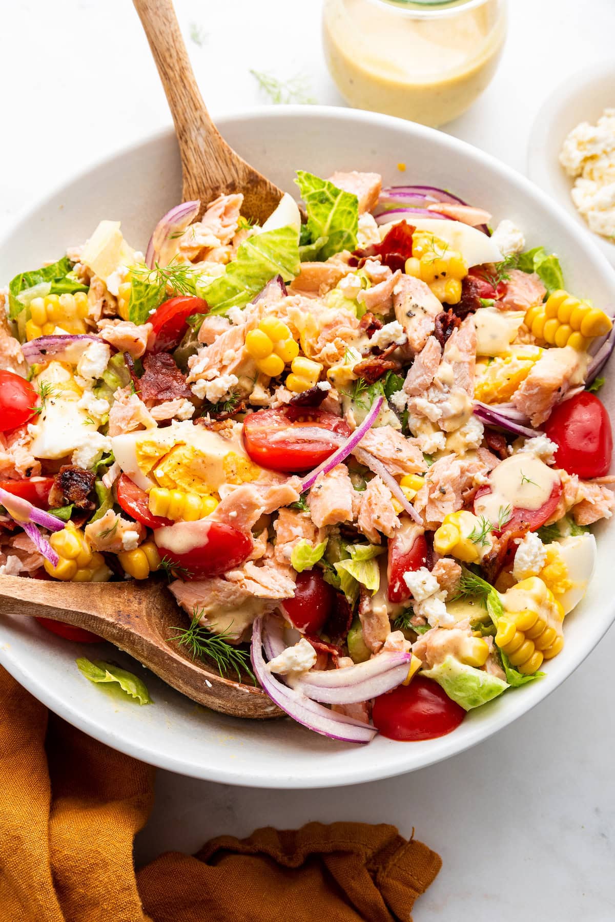 A salmon cobb salad in a large bowl with two wooden serving spoons.