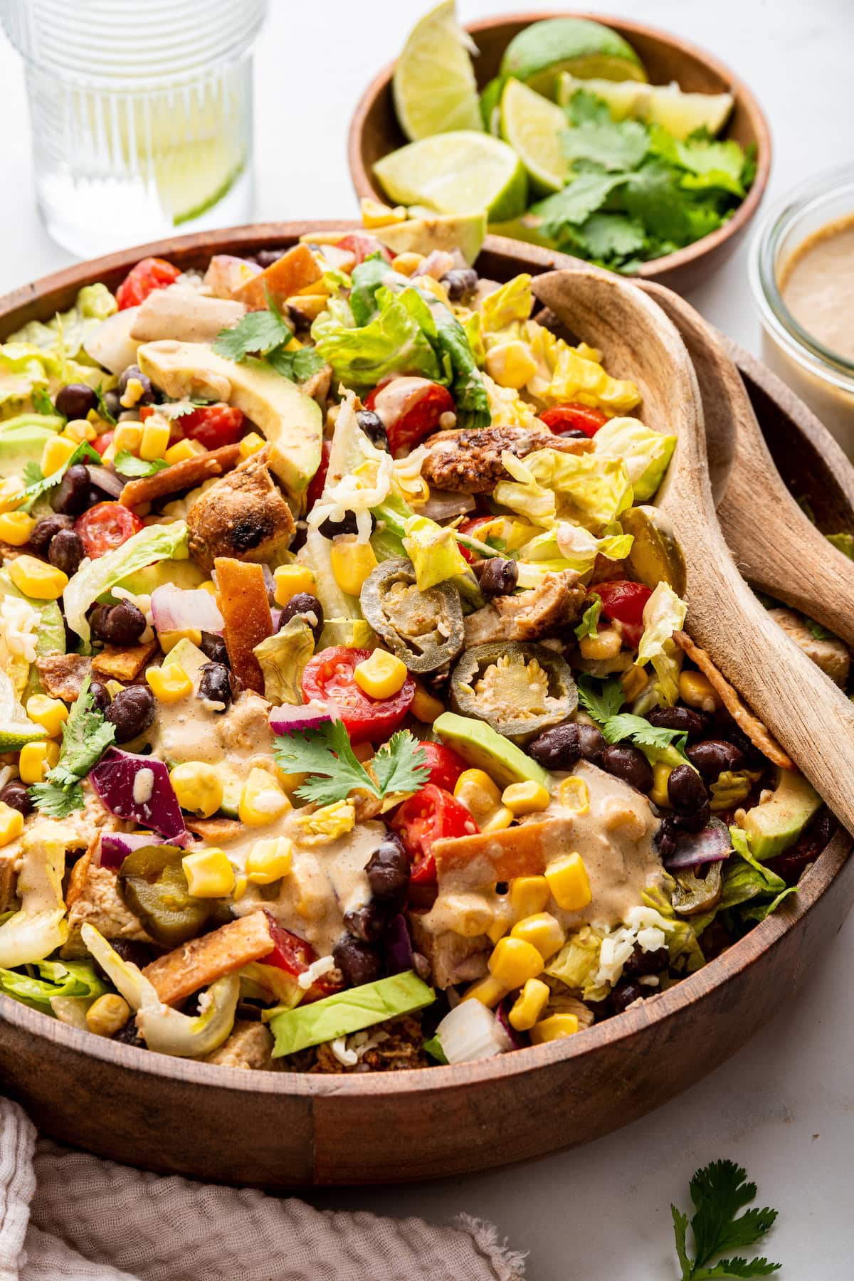 A southwest chicken salad in a large wooden bowl with two wooden serving spoons inside.