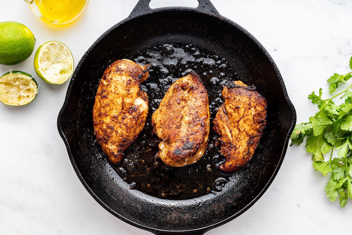 Three chicken breasts are being cooked in a cast iron skillet.