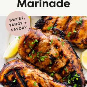Grilled marinated chicken on a plate, garnished with lemon and herbs.