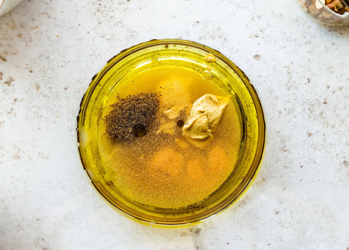 A blender with olive oil, vinegar, maple syrup, dijon mustard, garlic powder, salt, and pepper.