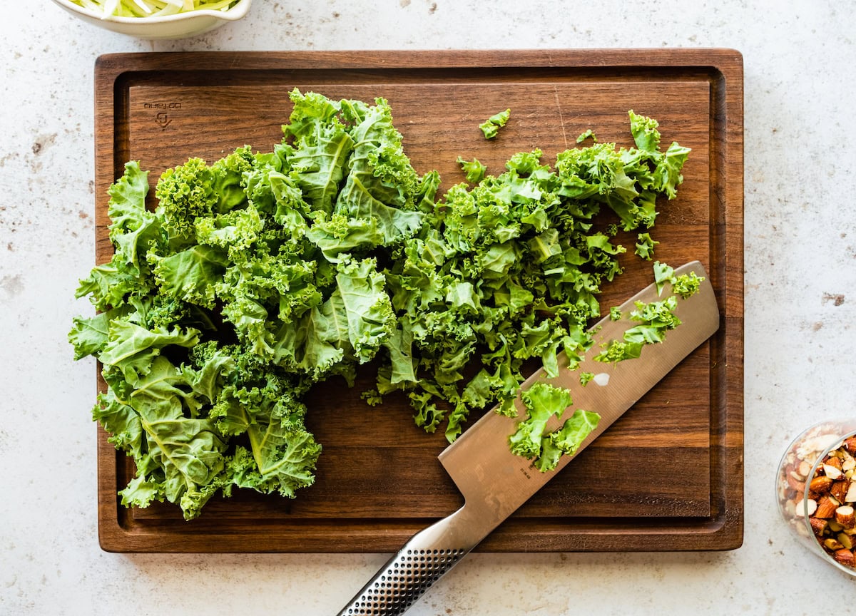 A wooden cutting board with a knife and chopped kale.