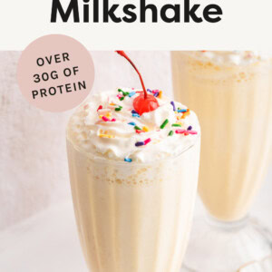 Protein Milkshake in a glass topped with whipped cream, sprinkles and a cherry.