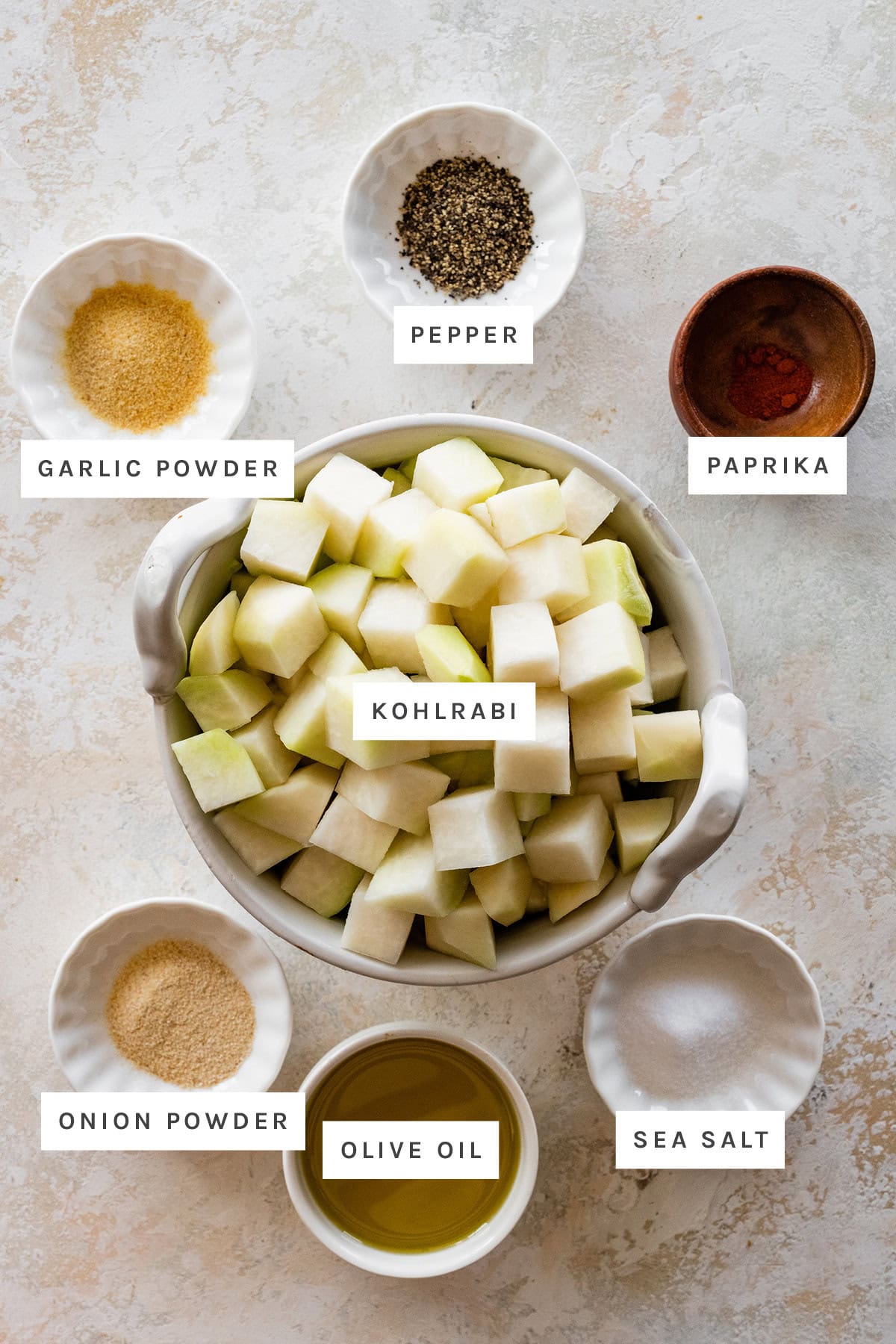 Ingredients measured out to make Roasted Kohlrabi: garlic powder, pepper, paprika, kohlrabi, onion powder, olive oil and sea salt.
