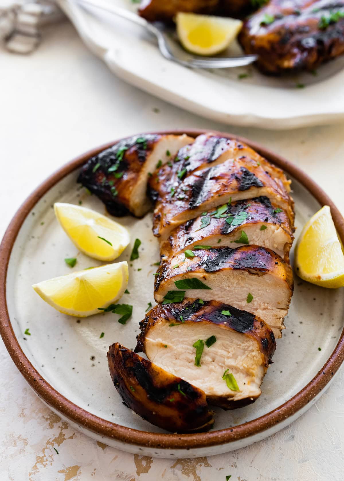 A marinated sliced chicken breast on a small plate with lemon wedges on the side.