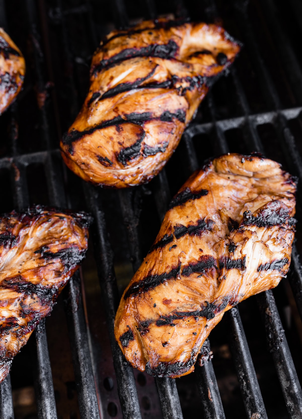 Four grilled and marinated chicken breasts on the grill.