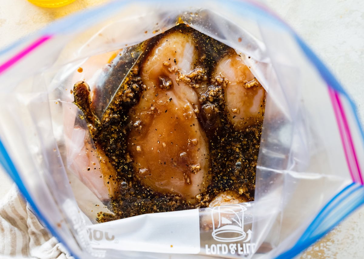 Four raw chicken breasts in a marinade in ziplock bag.