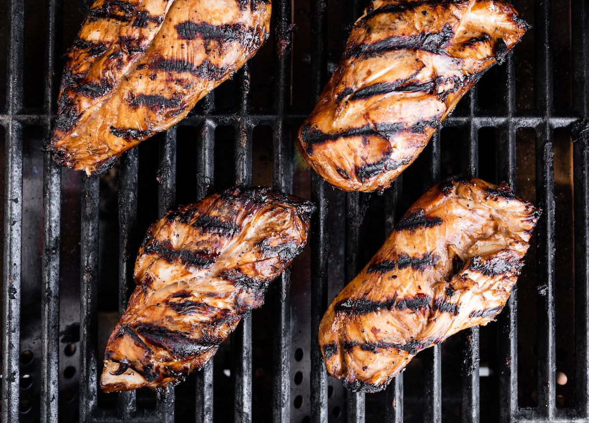 Four marinated chicken breasts cooking on a grill.
