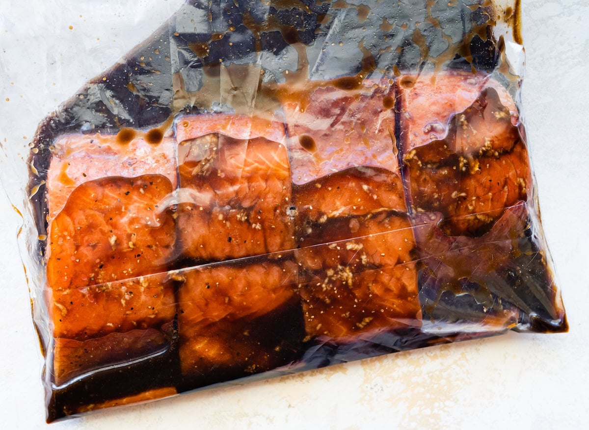 Four raw salmon filets in a bag of marinade.
