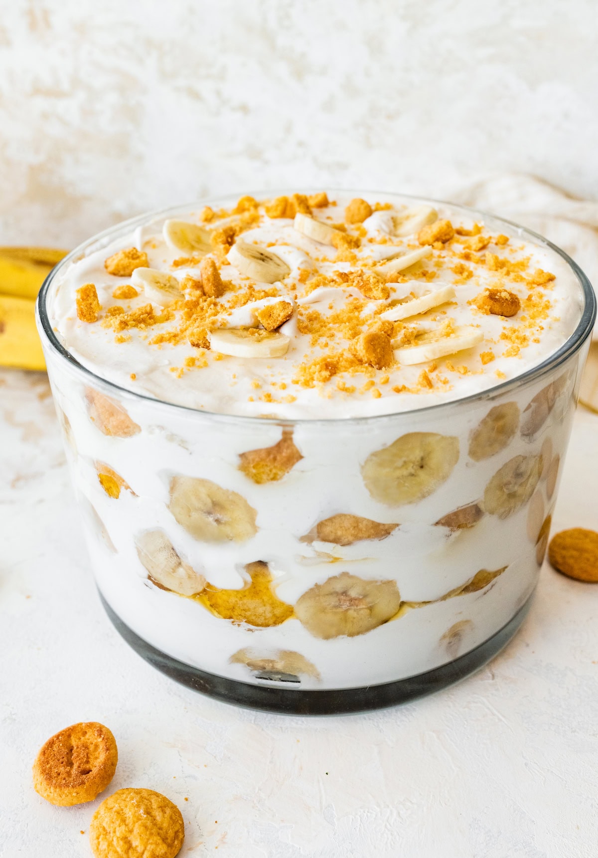 A glass trifle dish filled with healthy banana pudding. Layers of fresh banana slices and wafer cookies are visible in between the yogurt and coco whip.