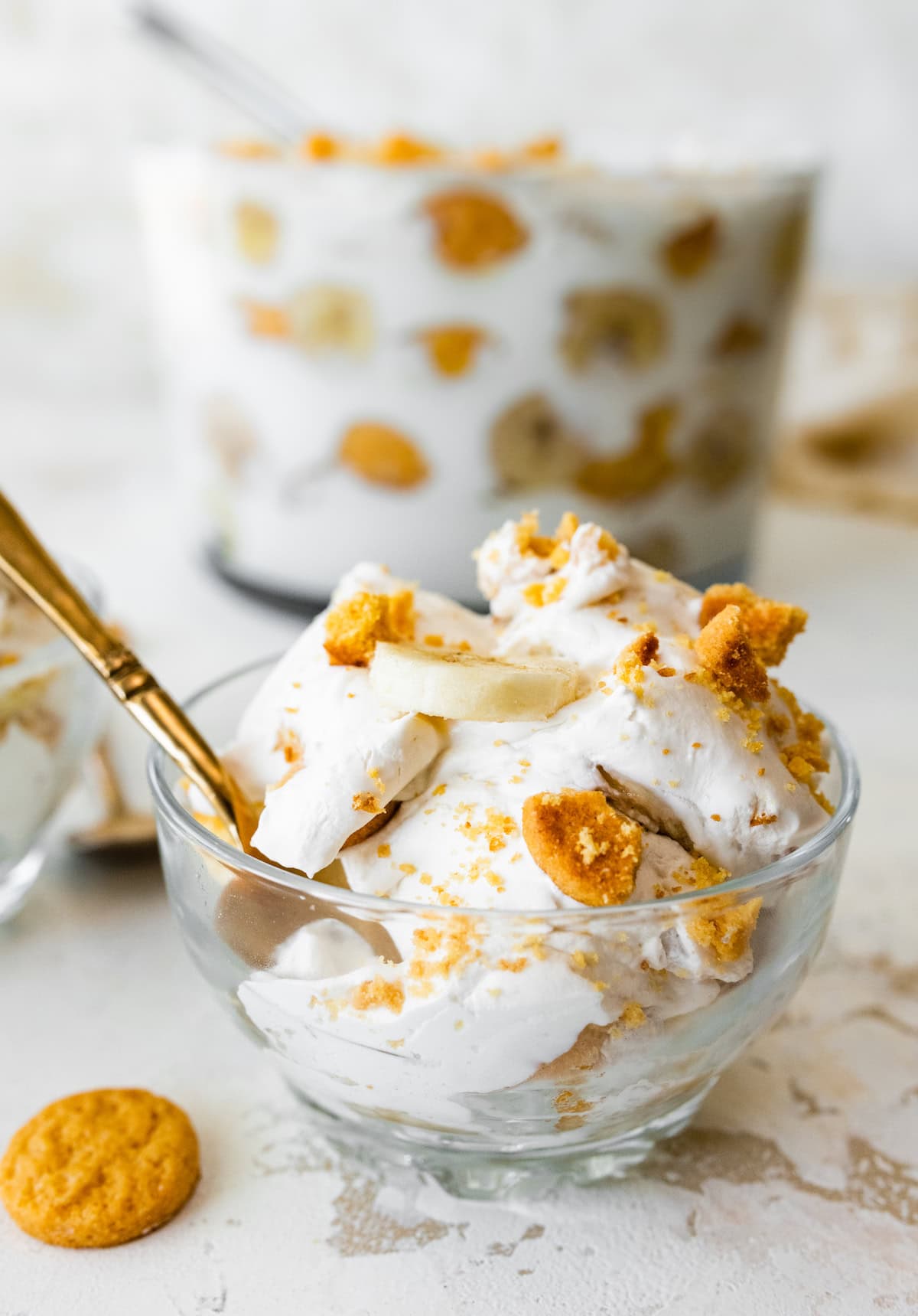 A small glass dish filled with banana pudding that's topped with fresh banana slices and crushed wafer cookies.