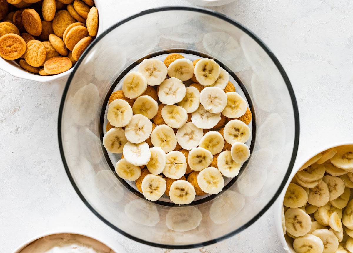 A layer of wafer cookies and fresh banana slices in the bottom of a glass trifle dish.