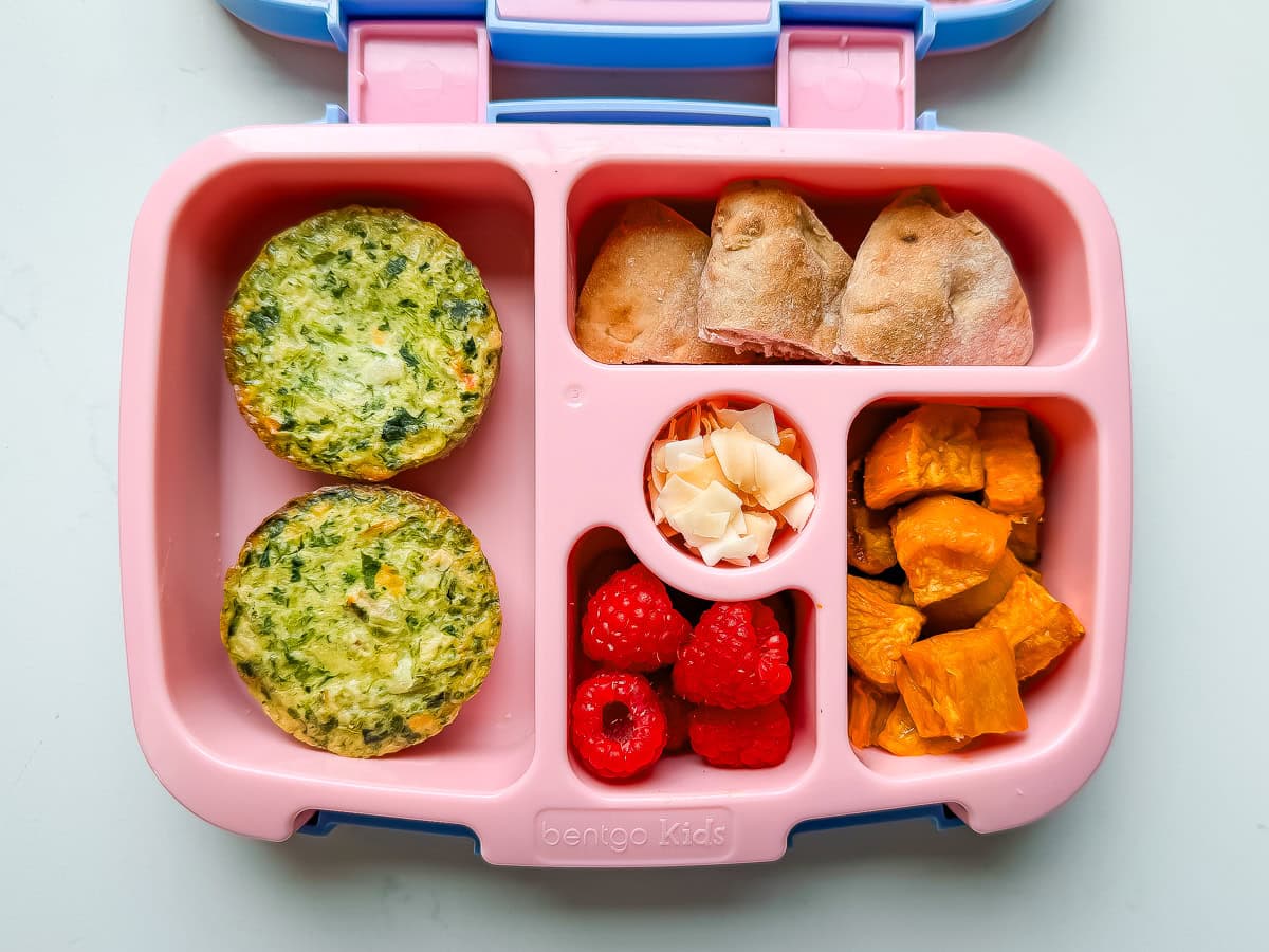 A pink Bentgo lunchbox packed with egg muffins, morning buns, toasted coconut flakes, roasted sweet potatoes and raspberries.