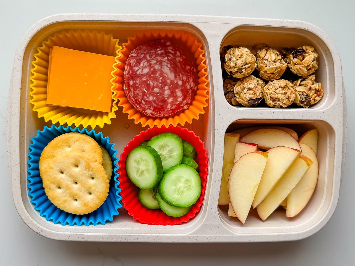 A DIY Lunchable with crackers, cheese, salami, cucumbers, granola minis and apple slices.
