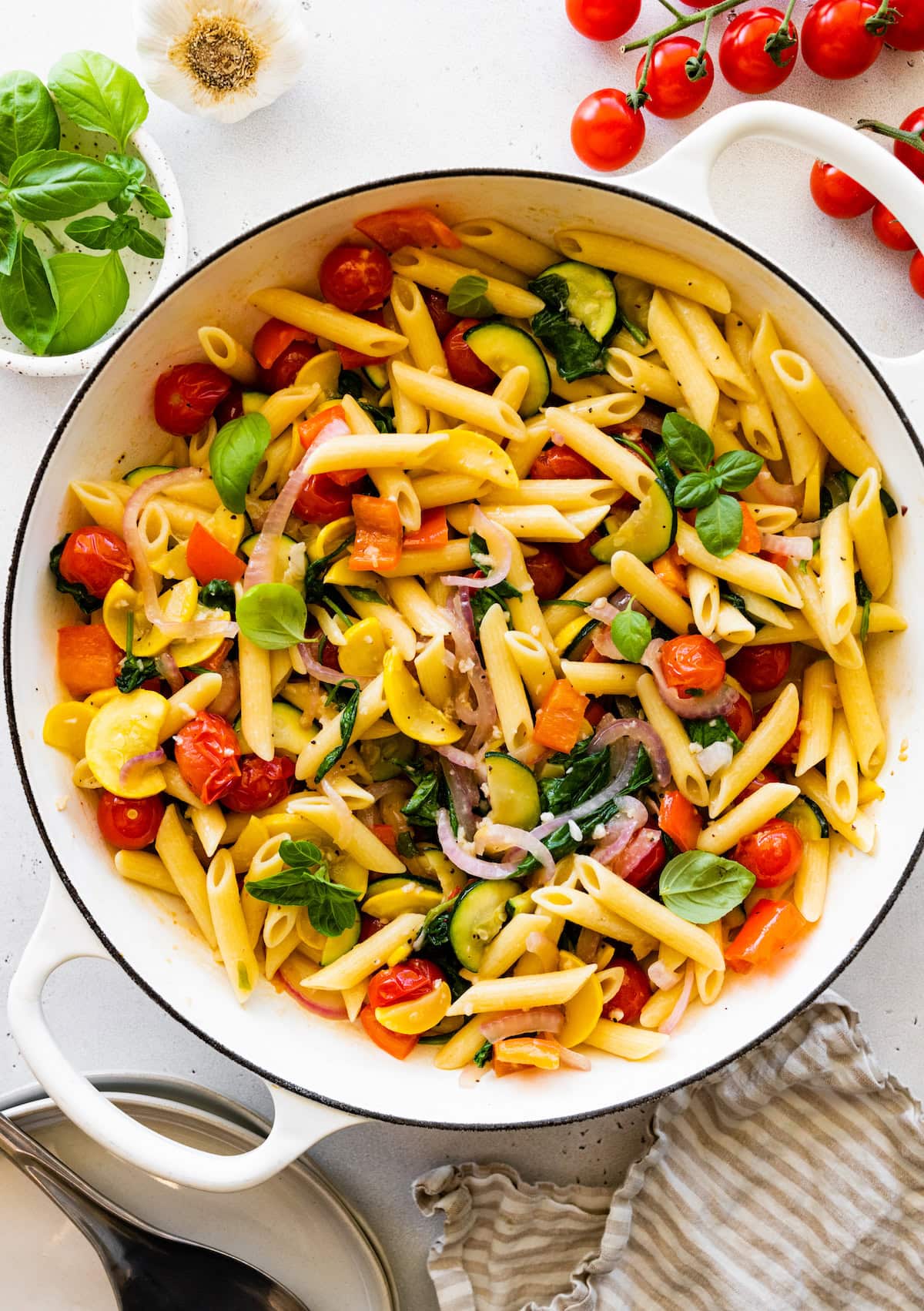 A large pot of cooked pasta with multiple vegetables including cherry tomatoes, squash, and spinach.