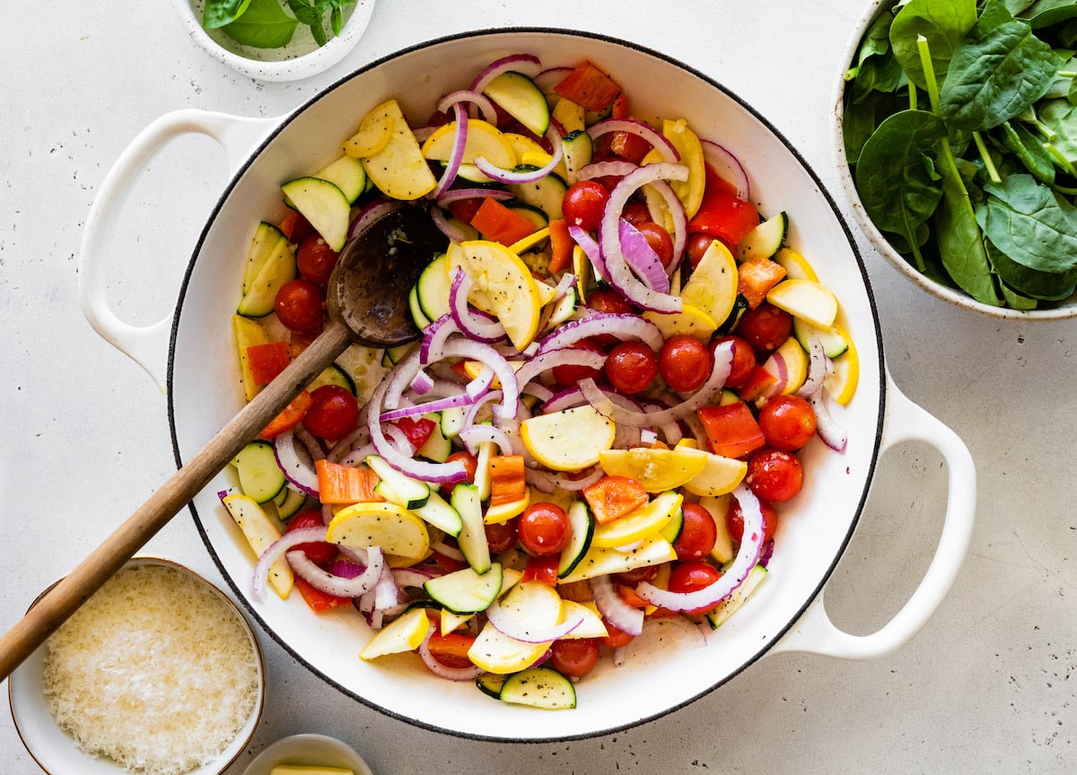 A large pot full of vegetables including cherry tomatoes, red onion, bell pepper, squash, and zucchini.