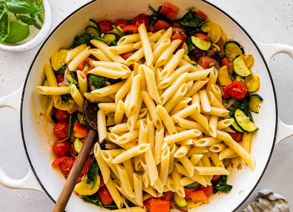 A large pot of cooked pasta with multiple vegetables including cherry tomatoes, squash, and spinach.
