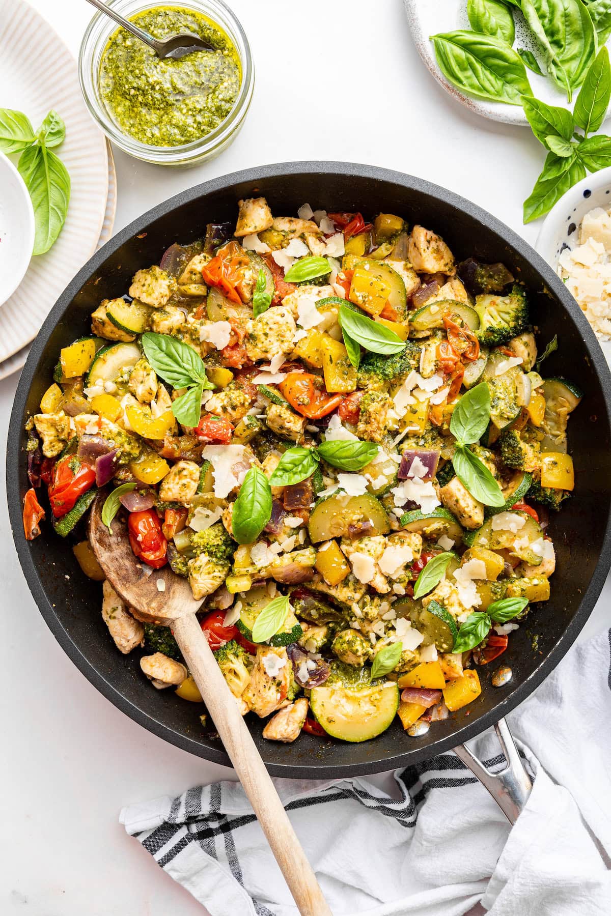 A large skillet with cooked pesto chicken, squash, cauliflower, cherry tomatoes, and fresh basil leaves.