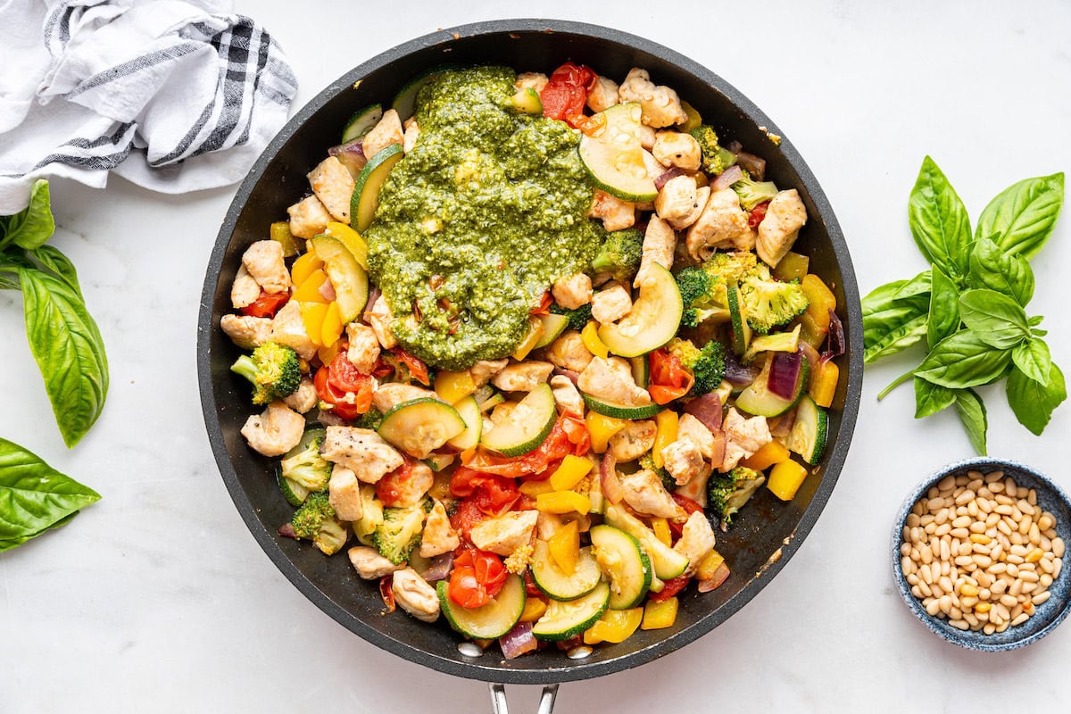 A large skillet with cooked chicken, squash, broccoli, cherry tomatoes, cauliflower, and pesto.