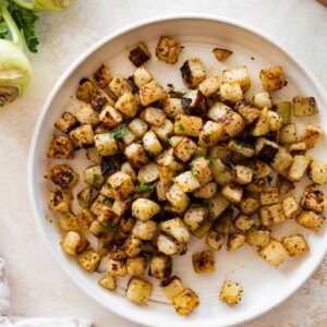 A plate of seasoned and roasted kohlrabi with a kohlrabi root near the plate.