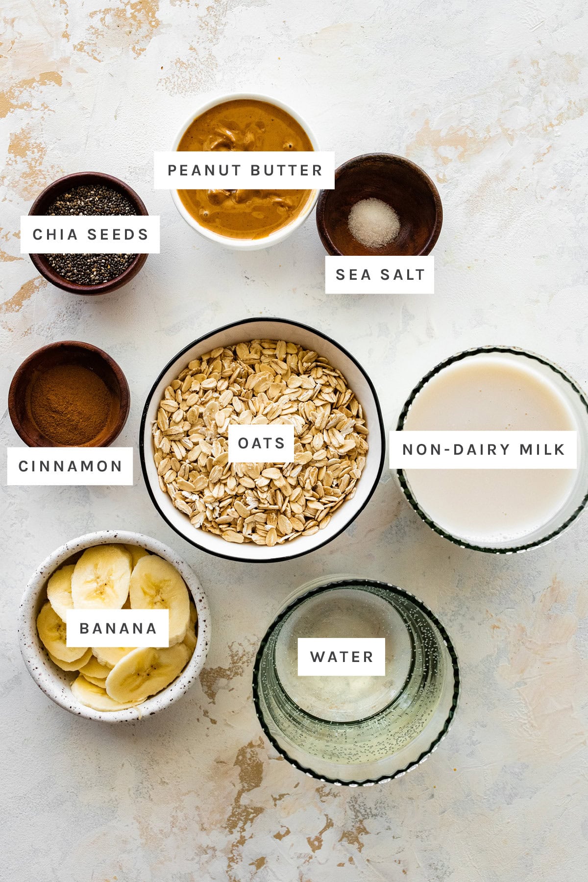 Ingredients measured out to make Peanut Butter Oatmeal: chia seeds, peanut butter, sea salt, cinnamon, oats, non-dairy milk, banana and water.