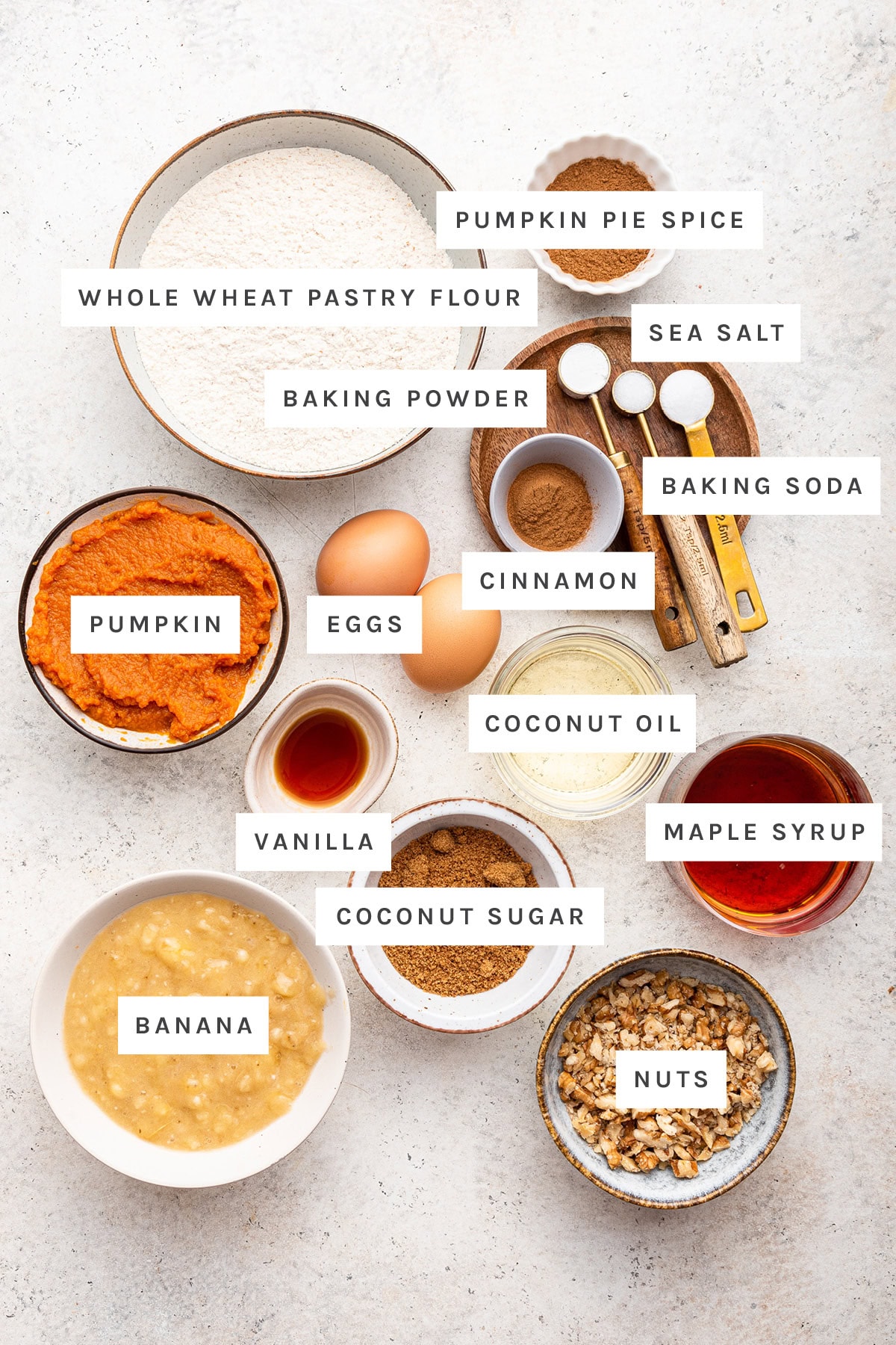 Ingredients measured out to make Pumpkin Banana Bread: whole wheat pastry flour, baking powder, pumpkin pie spice, baking soda, cinnamon, sea salt, vanilla, pumpkin, eggs, unsweetened applesauce, maple syrup, coconut sugar and coconut oil.