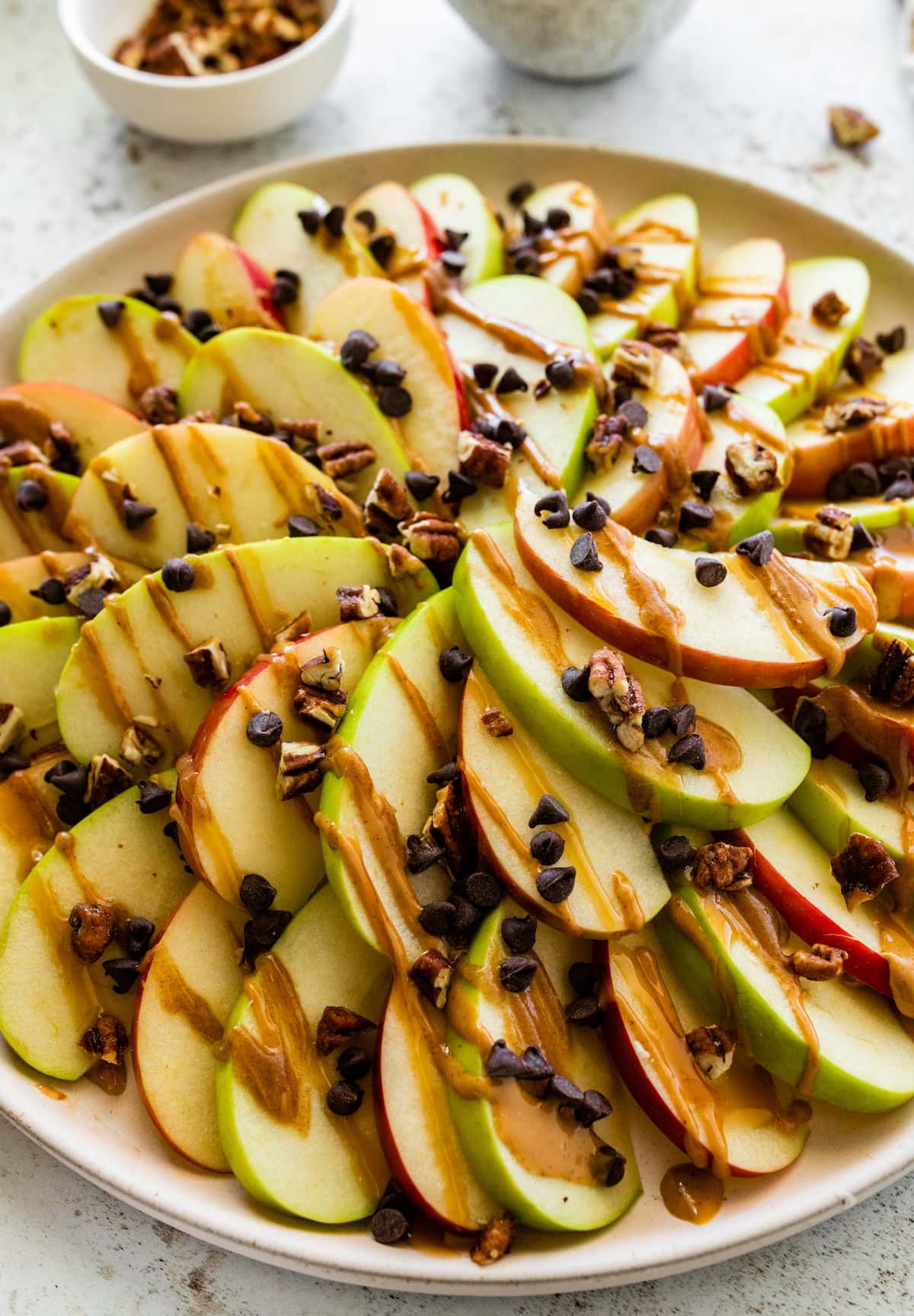 Apple slices on a plate topped with a drizzle of date caramel, mini chocolate chips, and pecans.