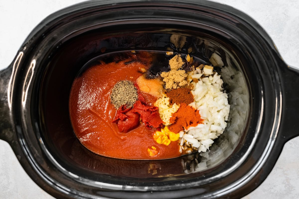 Many spices, tomato paste, bbq sauce, and diced onion in a slow cooker.