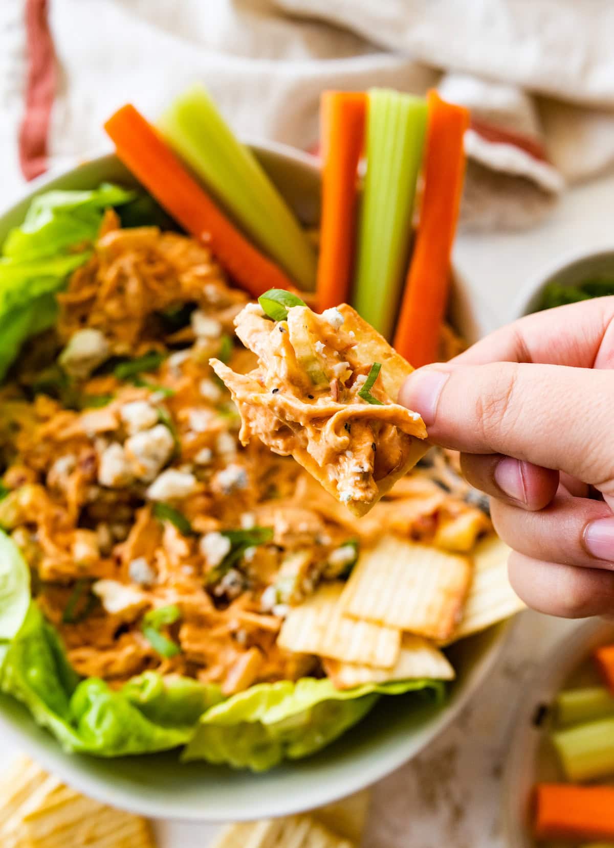 A woman's hand holds a cracker with a small portion of buffalo chicken salad on it.