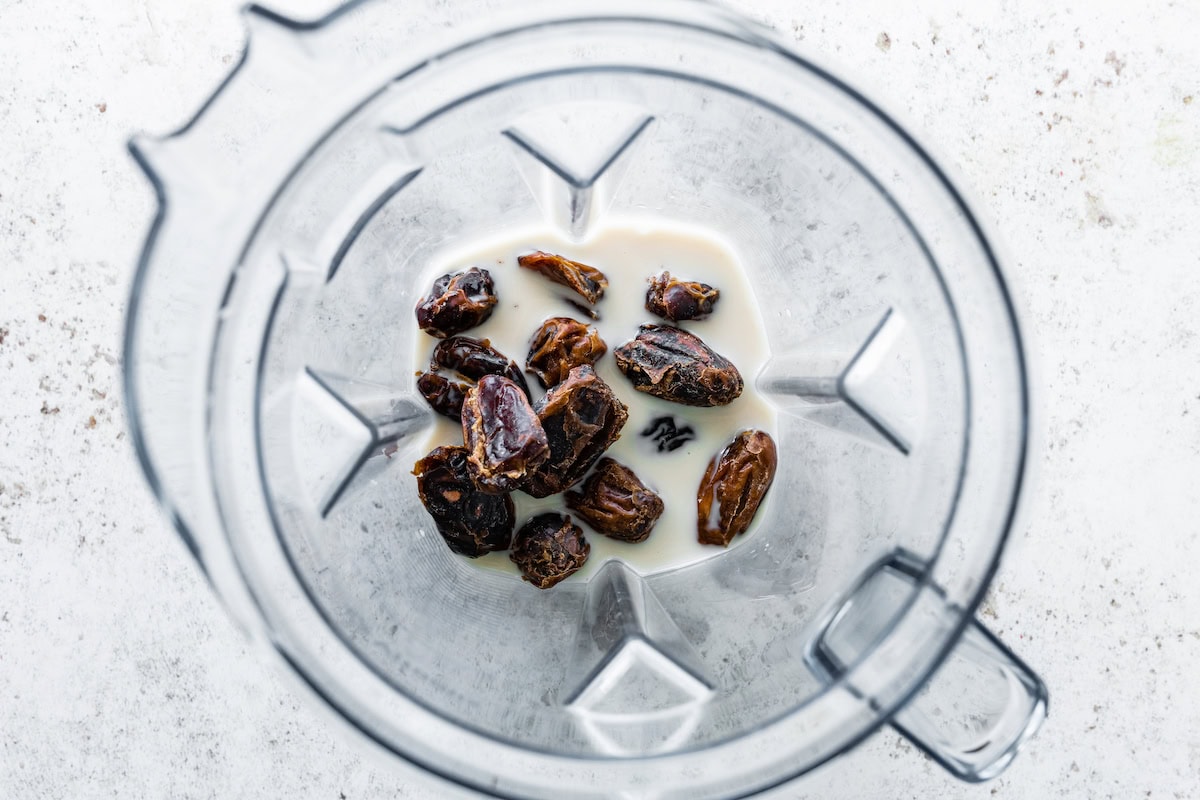 Multiple Medjool dates in a blender with almond milk.
