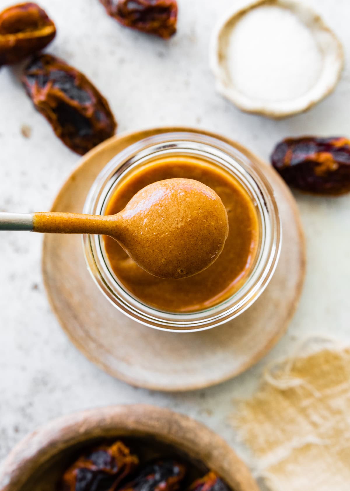 A spoonful of date caramel is held over a glass jar of the caramel.