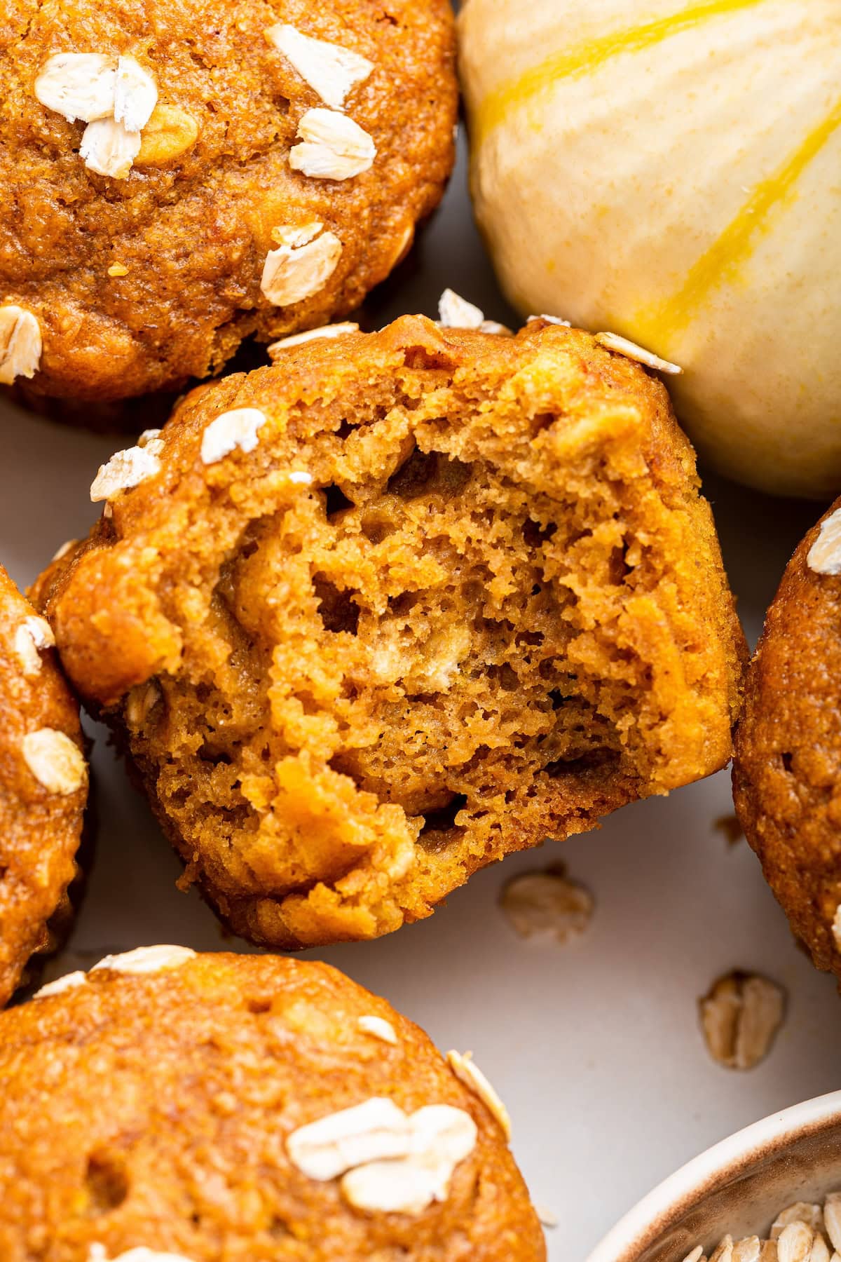A pumpkin muffin with a bite taken from it near other muffins.