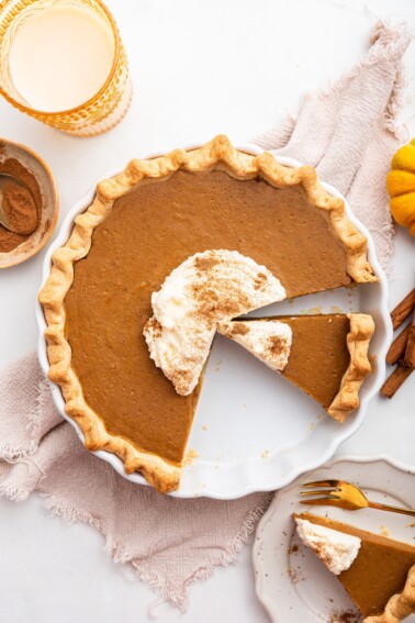 Healthy Pumpkin Pie topped with some whipped cream and cinnamon. A few slices are cut from the pie.