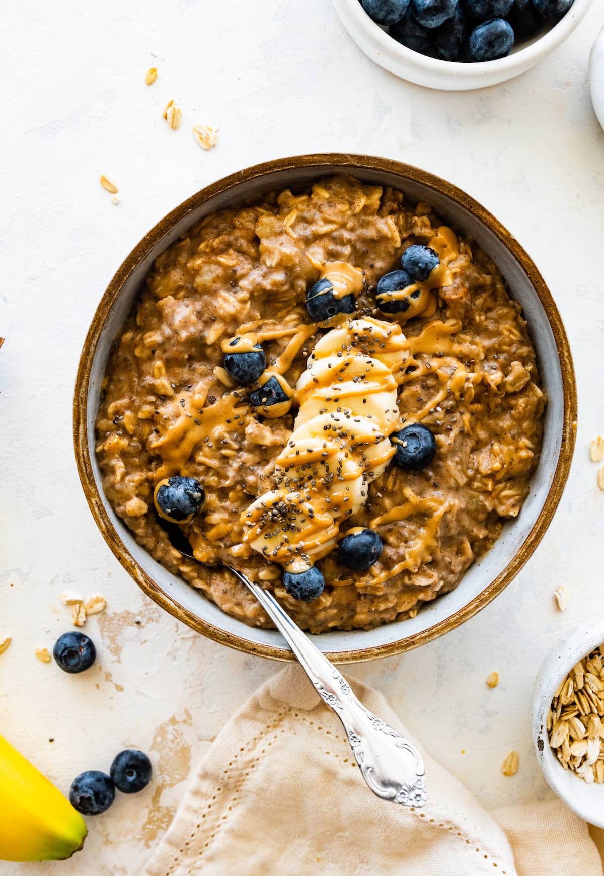 Peanut butter oatmeal in a bowl topped with banana, blueberries, peanut butter, and chia seeds.