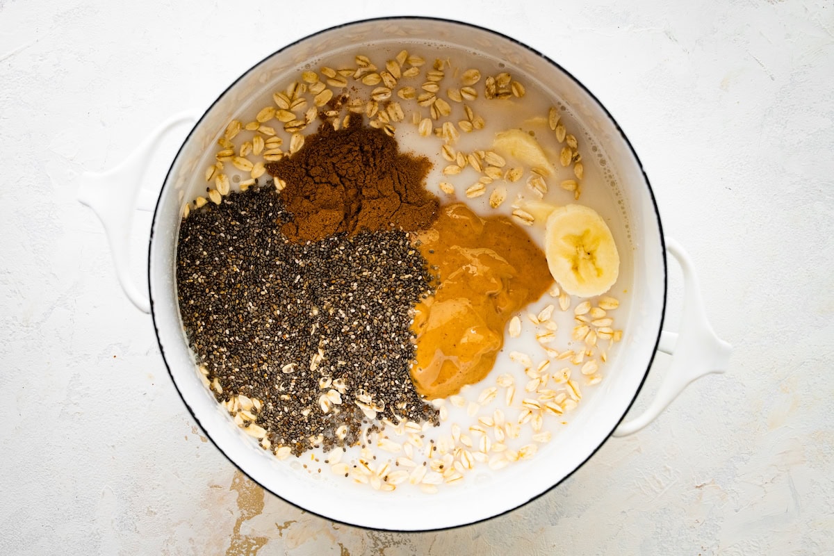 Ingredients for peanut butter oatmeal (rolled oats, chia seeds, peanut butter, banana, milk and cinnamon) in a pot.