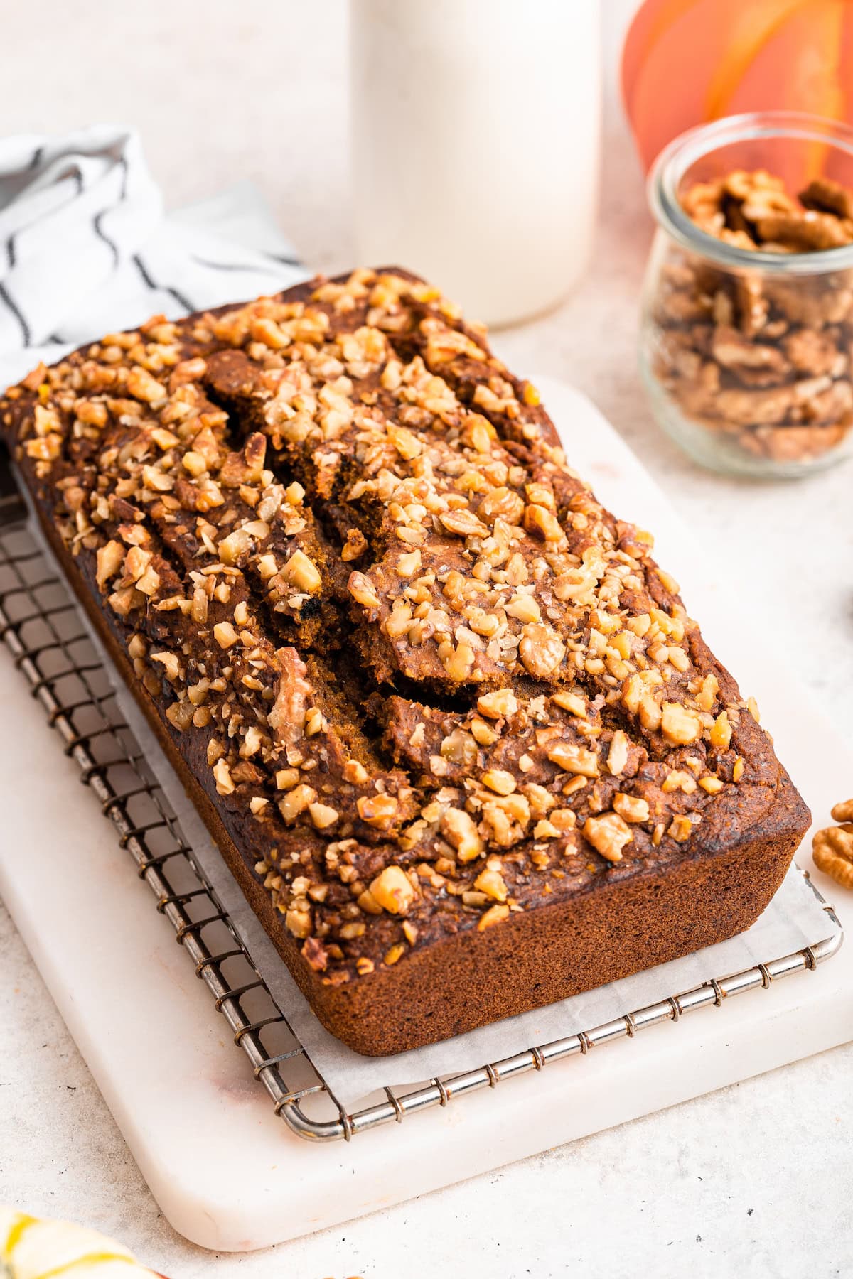 An unsliced loaf of pumpkin banana bread topped with chopped walnuts served on a wire rack.
